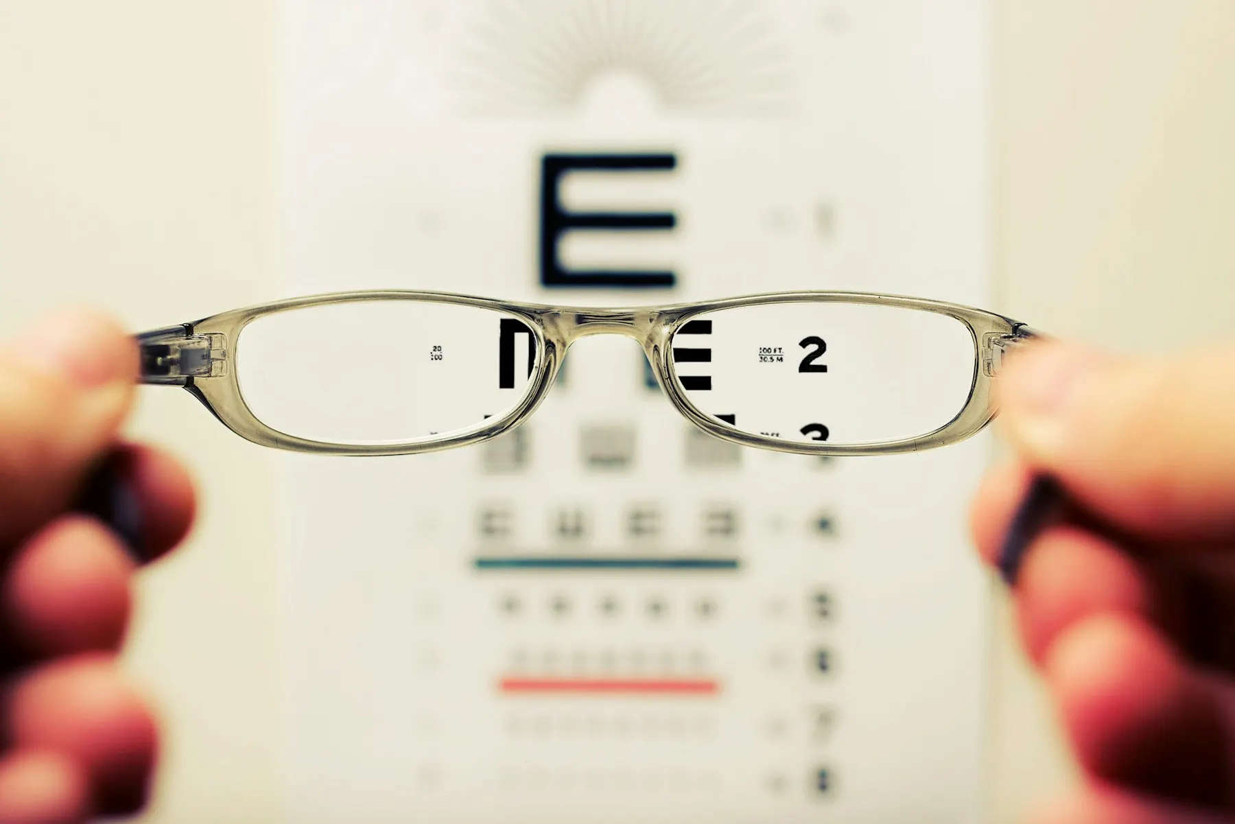 Glasses held in front of an eye chart, bringing the letters into focus